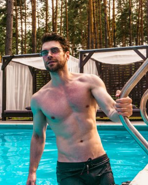 Yüzme havuzunda dinlenen, güneş gözlüğü takan gülümseyen adam. Yaz zamanı, tatiller, yaşam tarzı konsepti