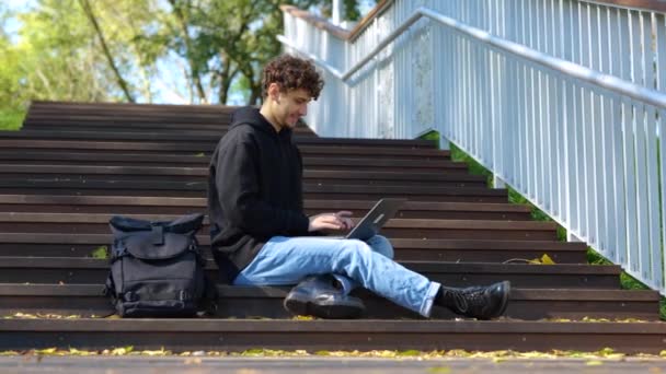 Smiling Stylish Guy Mengetik Laptop Sambil Duduk Tangga Taman Musim — Stok Video
