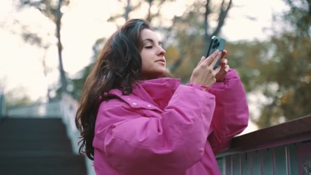 スタイリッシュな若い女性が携帯電話で写真を撮り 市立公園に立っています 季節のスタイル 秋の季節のコンセプト スローモーション — ストック動画