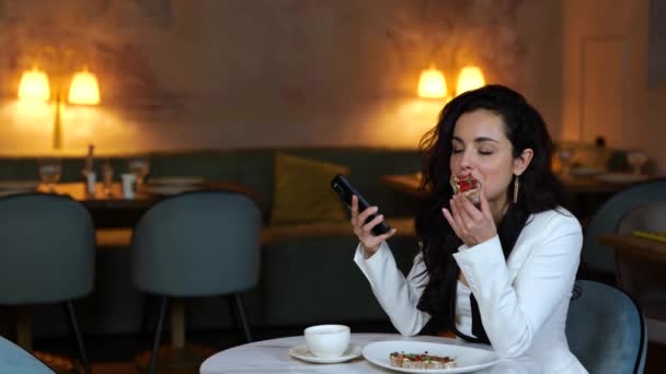 Красивая Женщина Наслаждается Обедом Ресторане Кусая Брускетту Держа Руках Смартфон — стоковое видео