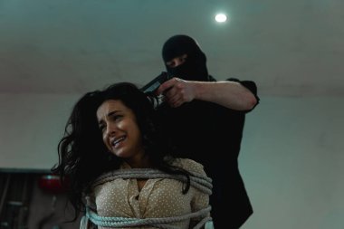 Siyah kar maskeli adam kaçıran kadın kafasına silah dayarken korkmuş bir kadın ağlıyor. Suç, adam kaçırma, şiddet kavramı