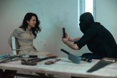 Kadın bodrumdaki sandalyeye iple bağlanmış ağlarken çocuk kaçıran kişi cep telefonunda video çekiyor. Suç, adam kaçırma, şiddet kavramı