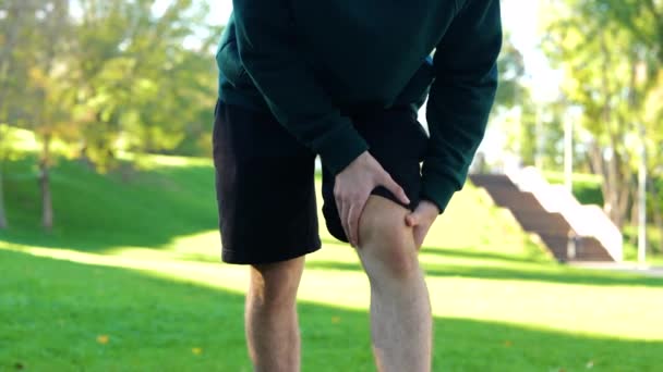 年轻人在绿地公园锻炼前按摩了一下膝盖和肌肉 运动员在户外活动前伸展身体 夏日晴天 年轻的高加索人站在外面 — 图库视频影像