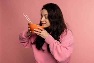 Kadının belden yukarı portresi. Pembe arka plandaki kameranın önünde seramik kasede nefis yemek kokusu soluyor.