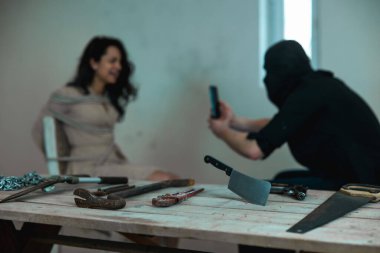 Siyah kar maskeli bir çocuk kaçıran, video çeken, sandalyeye iple bağlanmış bir kadın kaçıran. Silahlara odaklan. Suç, adam kaçırma, şiddet kavramı