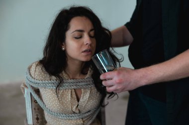 Sandalyeye oturup halatla bağlanmış tükenmiş bir kadın, onu kaçıran erkek ona su veriyor. Suç, adam kaçırma, şiddet kavramı