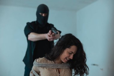 Korkmuş bir kadın bodrumda silahını ona doğrultup ağlarken iple bağlanmış bir şekilde oturuyor. Suç, adam kaçırma, şiddet kavramı