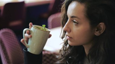 Yakın çekim, yavaş çekim. Kafenin içinde oturmuş, naneli sıcak çay içen, uzun kahverengi saçlarına dokunan, gülümseyen ve çok mutlu ve başarılı görünen beyaz bir kız..