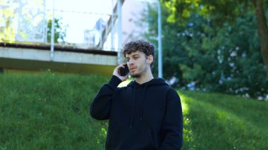 Genç adam parkta poz verirken cep telefonuyla konuşuyor ve kötü haberler alıyor. Yaşam tarzı. Sonbahar yürüyüşü kavramı. Yavaş çekim