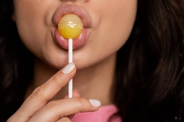 Close up of a female with sensual plump lips and perfect skin sucking a delicious yellow lollipop on the plastic stick. Self-indulgence concept