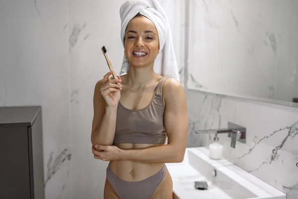 Waist up photo of sexy young woman in underwear posing near the washbasin with a mirror and holding her toothbrush. Routine, self-care, lifestyle concept