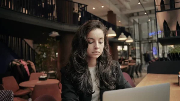 Close up, slow motion. Caucasian Businesswoman working on her computer inside of modern restaurant. Girl working remotely, outside her office. Woman looking into the window, thinking and looks serious