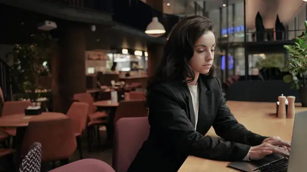 Businesswoman sitting in the restaurant and working on her computer. Young Caucasian woman sitting in the cafe at a wooden table, girl is typing on her laptop and she looks very tired.