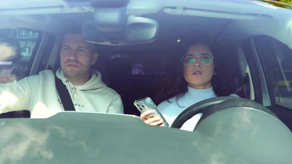 close up of Caucasian young couple man and woman in car. Beautiful attractive stylish female driving a car and tapping on smartphone. Male and female travel in auto. Trip concept, slow motion