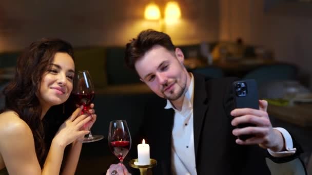 レストランのロマンチックなディナーの間にかわいい女性とセルフィーを作っている間 携帯電話を持っている笑顔の若い男 ライフスタイル 人間関係の概念 スローモーション — ストック動画