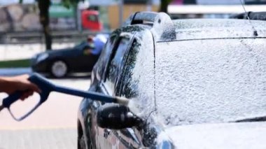 Erkek, arabasını oto yıkamada yıkıyor ve tazyikli köpüklü hortum kullanıyor. self servis, araba yıkama konsepti. Gerçek zamanlı.