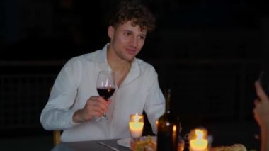 Genç adam elinde bir kadeh kırmızı şarap tutarken ve kız arkadaşıyla konuşurken dışarıda eğleniyor. Çatıda romantik bir randevu. Romantik bir kavram. Birbirine aşık bir çift. Gerçek zamanlı.