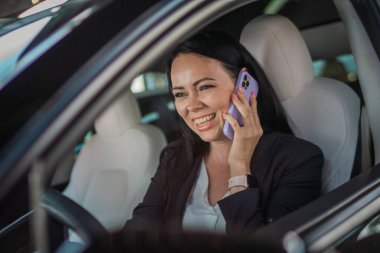 Çalışırken araba süren ve cep telefonuyla konuşan gülümseyen genç iş kadını. İş, yolculuk, teknoloji, seyahat kavramı