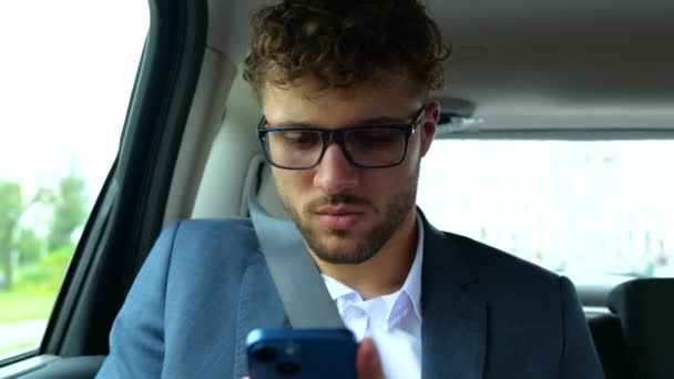 穿着西服的年轻人坐在汽车后座上 一边用智能手机打字 运输和技术概念 慢动作 — 图库视频影像