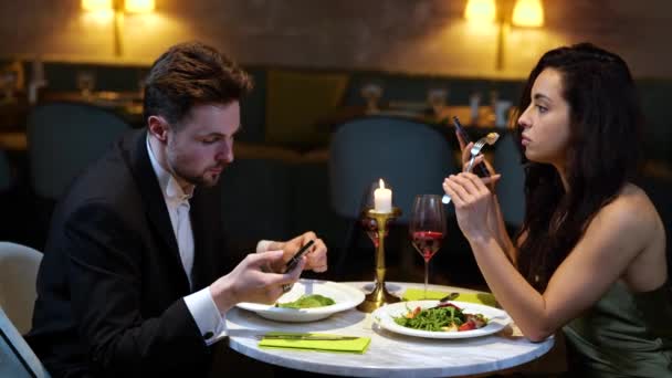 携帯電話を使用しながらレストランでおいしいサラダを楽しんでいる若い男女 ライフスタイル 人間関係の概念 スローモーション — ストック動画