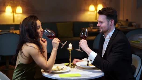 笑顔のロマンチックな男と女性がレストランでワイングラスを飲みます ウェイトレスはテーブルからプレートを取る ライフスタイル 人間関係の概念 スローモーション — ストック動画
