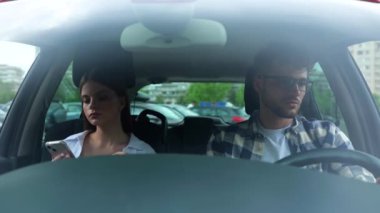 Genç bir kadın yolcu koltuğunda oturup telefon ekranına bakarken erkek sürücü araba kullanıyor. Ulaşım, seyahat, ilişkiler, güvenlik kavramı. Yavaş çekim