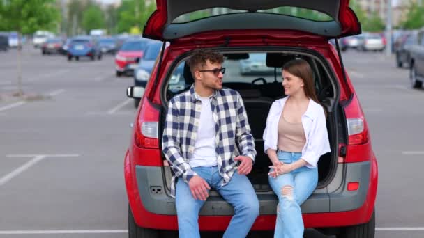 年轻夫妇坐在行李箱上聊天的时候 笑着一起在外面的车里呆着 公路旅行 旅行和生活方式的概念 慢动作 — 图库视频影像