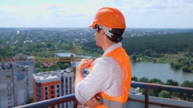 Foreman inşaat üniforması ve güvenlik kaskı takıyor ve inşaat alanının çatısında duruyor. İş, inşaat, endüstri konsepti. Yavaş çekim