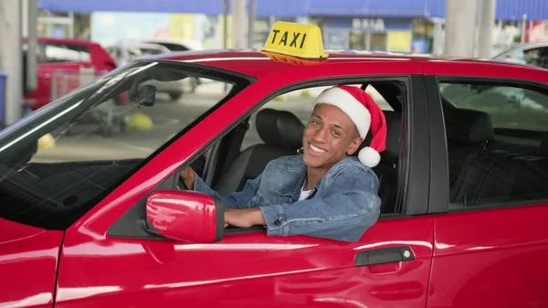 Happy young male taxi driver wearing Christmas Santa hat and showing thumbs up, looking out the open window. Winter holidays celebration concept. Slow motion