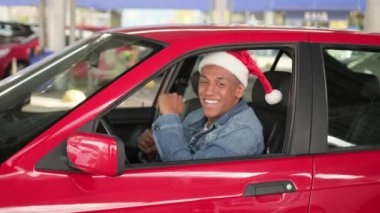 Noel Baba şapkalı mutlu Afrikalı Amerikalı adam dans ederken müziğin tadını çıkarıyor, araba camından dışarı bakıyor. Kış bayramı kutlaması. Yavaş çekim