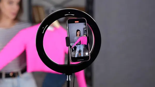 Display of mobile phone screen recording video blog. Female blogger holding and showing pink jumper to followers.Vlogging concept. Slow motion video