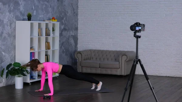 Sporty young lady exercising in the living room at home while doing burpee, training and making functional workout. Female recording sports video for vlog