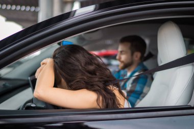 Genç adam arabada yolcu koltuğunda otururken kadın başını direksiyona yaslıyor. Seyahat macerası, mutlu yaz tatili konsepti