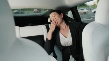 Yorgun iş kadını arka koltukta uyurken dinleniyor, araba yolculuğu sırasında esniyor. Ulaşım, seyahat, iş konsepti. Yavaş çekim