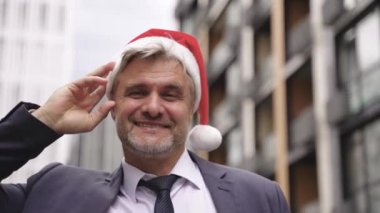 Noel Baba şapkalı, gülümseyen yetişkin bir beyaz adam başparmağını kaldırarak sokakta dikiliyor. Kutlama, Noel, tatil, iş konsepti. Yavaş çekim