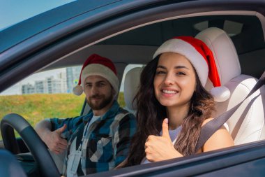 Gülümseyen kız öğrenci ve erkek eğitmen arabada oturuyor ve Noel Baba şapkası takarken başparmağını bırakıyor. Noel, tatil, test sürüşü, sınav, eğitim konsepti