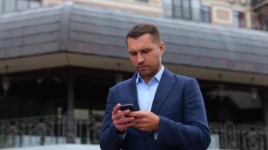 Akıllı telefon kullanarak şehirde yürüyen yakışıklı beyaz erkek portresi. Genç başarılı beyefendi cep telefonundan mesaj yolluyor. Teknoloji, iletişim konsepti. Gerçek zamanlı konsept