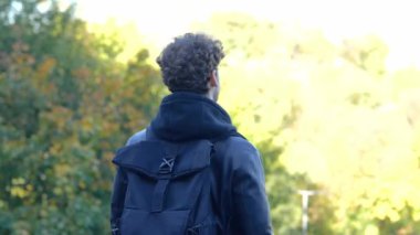 Siyah sırt çantalı şık adam sonbahar parkında manzarayı seyrediyor. Arkadan bak. Sonbahar yürüyüşü kavramı. Gerçek zamanlı konsept.