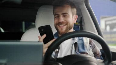 Arabada oturmuş telefonda mesaj okurken gülümseyen başarılı genç adam. Yaşam tarzı, teknoloji, yolculuk konsepti. Yavaş çekim