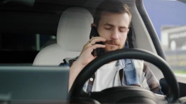 Arabada sürücü koltuğunda otururken akıllı telefondan konuşan beyaz bir adam. Yaşam tarzı, teknoloji, yolculuk konsepti. Yavaş çekim
