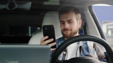 Arabada sürücü koltuğunda otururken cep telefonu kullanan mutlu adam. Yaşam tarzı, teknoloji, yolculuk konsepti. Yavaş çekim