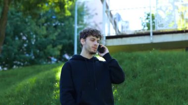 Genç adam parkta poz verirken cep telefonuyla konuşuyor ve kötü haberler alıyor. Yaşam tarzı. Sonbahar yürüyüşü kavramı. Gerçek zamanlı konsept.