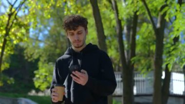 Şehir parkında yürürken kahve içip cep telefonuyla konuşan mutlu adam. Yaşam tarzı. Sonbahar yürüyüşü kavramı. Gerçek zamanlı konsept.