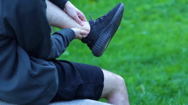 穿着黑斑短裤 运动鞋的运动员放松 按摩他的腿 感觉腿疼痛 侧视年轻的白人男子坐在水泥长椅上 锻炼后腿受伤 — 图库视频影像