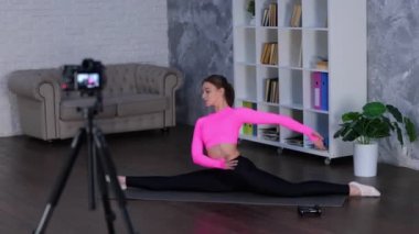 Tozluklu ve üstsüz atletik kadın sicimin üzerinde otururken kadın evde yoga egzersizi yapıyor. Tripodun üzerinde kamera kullanan bir kadın. Spor salonu, spor konsepti. Gerçek zamanlı video.