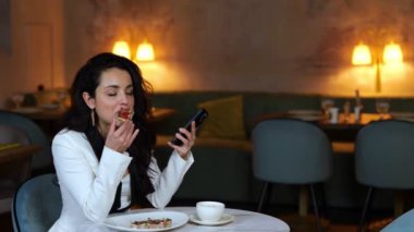Güzel bir kadın restoranda bruschetta yerken ve elinde akıllı telefon tutarken öğle yemeğinden zevk alıyor. Uzayı kopyala İş, yaşam tarzı konsepti. Gerçek zamanlı video.