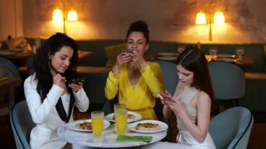 Kadın arkadaşlar cep telefonu kullanırken yemek fotoğrafları çekiyorlar, restoranda yemek yiyorlar. Arkadaşlarla buluşacağız. Yaşam tarzı, arkadaşlık kavramı. Gerçek zamanlı video.