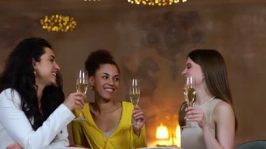 Modern restoranda yemek yerken kadehlerini şampanyayla tokuşturan üç genç kadın. Arkadaşlarla buluşacağız. Yaşam tarzı, arkadaşlık kavramı. Gerçek zamanlı video.