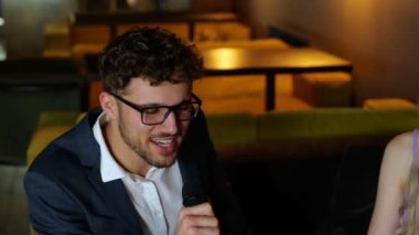 Gözlüklü, gülümseyen şık adam restoranda oturmuş karaoke şarkıları söylüyor, arkadaşları da müziğin keyfini çıkarıyor. Yaşam tarzı, parti konsepti. Gerçek zamanlı..