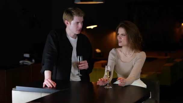 Молодой человек и женщина ссорятся, сидя в ресторане с бокалами шампанского. Стиль жизни, отношения, концепция свидания. В реальном времени.